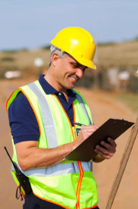 A man in yellow hard hat writing on paper.