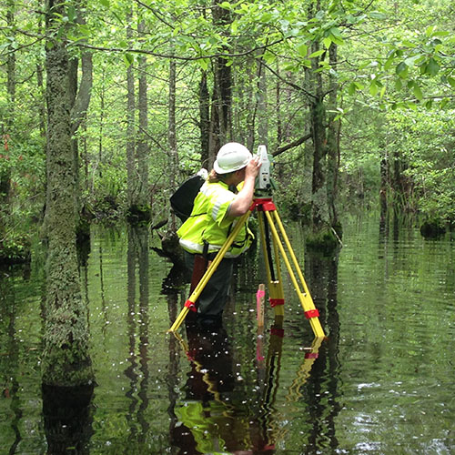A man in the water using a surveying tool.