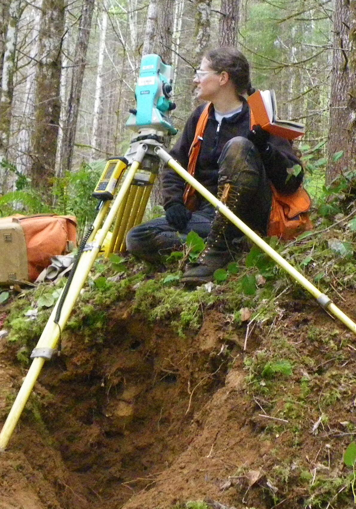 A woman sitting on the ground with a surveying equipment.